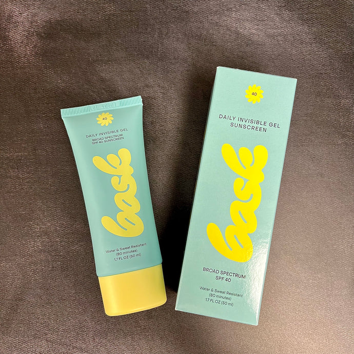 A blue and yellow tube of sunscreen with a blue and yellow box to its right, both read Bask daily invisible gel sunscreen broad spectrum SPF 40. Sold at Coyote Supply Co a BIPOC and LGBTQIA+ owned zero waste witch store in Reno Nevada 