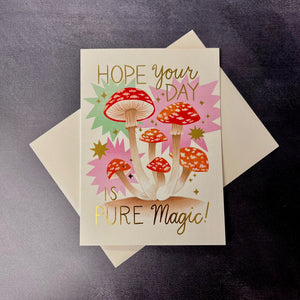 A cream card with red and white mushrooms and gold foil text that reads Hope your day is pure magic! on a white envelope. Sold at Coyote Supply Co a BIPOC and LGBTQIA+ owned zero waste witch store in Reno Nevada 