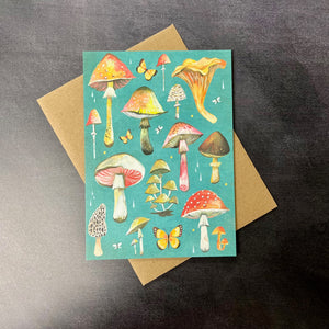 A teal card with illustrations of many different colorful mushrooms and butterflies on a brown kraft envelope. Sold at Coyote Supply Co a BIPOC and LGBTQIA+ owned zero waste witch store in Reno Nevada 