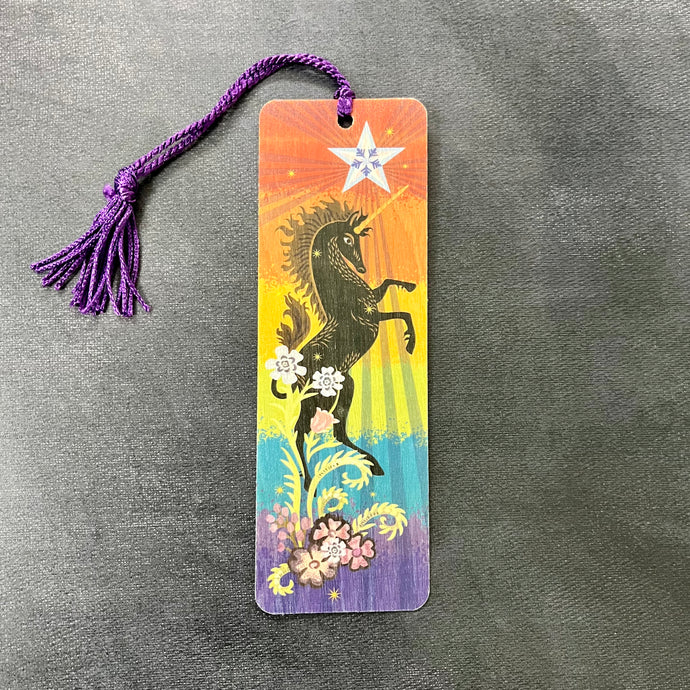 A vibrant rainbow wood bookmark with a purple tassel featuring an image of a black unicorn under a trans pride star. Sold at Coyote Supply Co a BIPOC and LGBTQIA+ owned zero waste witch store in Reno Nevada