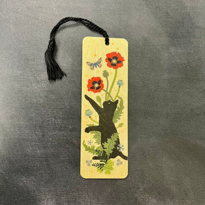 A light wood bookmark with a black tassel featuring an image of a black cat playing in poppies chasing a butterfly. Sold at Coyote Supply Co a BIPOC and LGBTQIA+ owned zero waste witch store in Reno Nevada