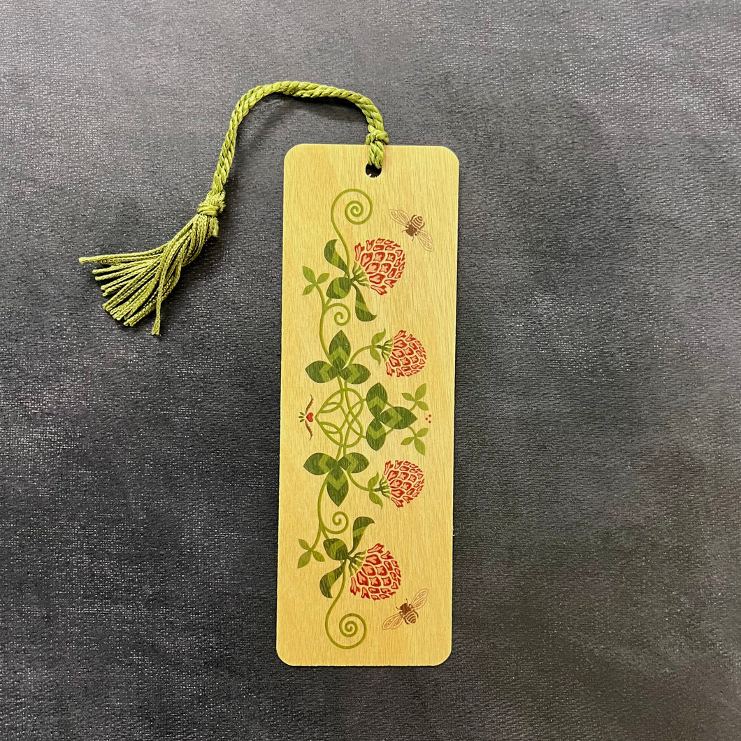 A light wood bookmark with a green tassel featuring an illustration of red clover and bees. Sold at Coyote Supply Co a BIPOC and LGBTQIA+ owned zero waste witch store in Reno Nevada