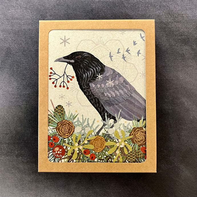 A light brown kraft box with a viewing window showing the design of the greeting cards inside, the cards depict a crow with a sprig of holly in their mouth surrounded by plants and pinecones. Sold at Coyote Supply Co a BIPOC and LGBTQIA+ owned zero waste witch store in Reno Nevada