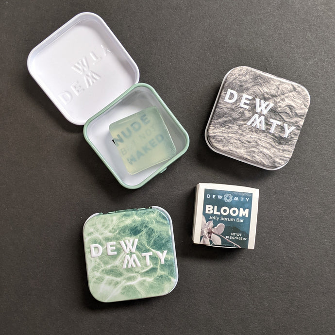 The DEW MTY Bloom jelly serum bar alongside it's packaging options of a paper wrap or metal case in green or grey. Sold at Coyote Supply Co a BIPOC and LGBTQIA+ owned zero waste witch store in Reno Nevada