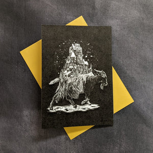 A black card with a monochrome illustration of a yule goat with a winter village on it's back by Death of Seasons on a yellow envelope. Sold at Coyote Supply Co a BIPOC and LGBTQIA+ owned zero waste witch store in Reno Nevada 